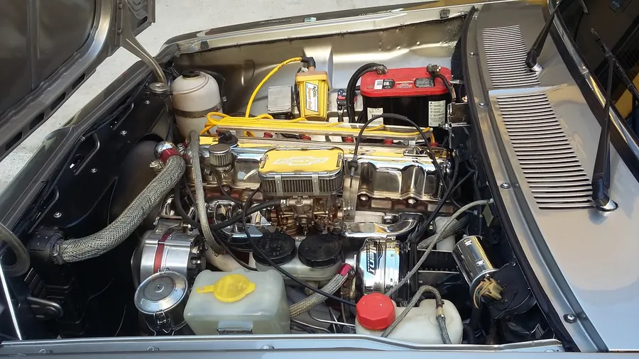 Motor de um carro clássico, com tampas cromadas e cabos amarelos